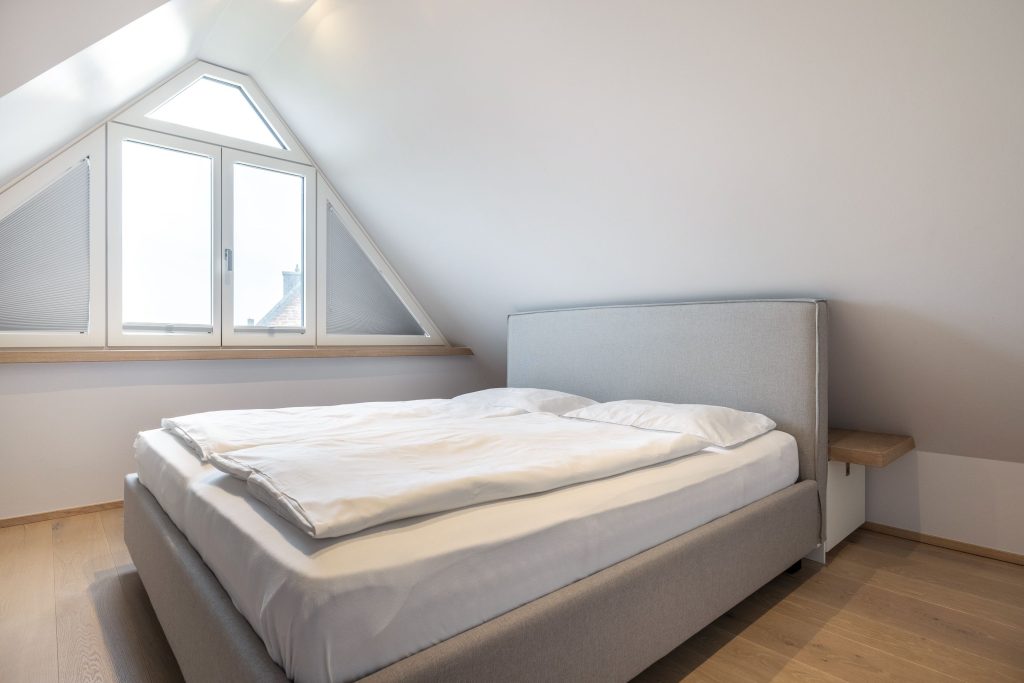 Schlafzimmer mit grauem Bett und großem Fenster in Ferienwohnung am Sylt